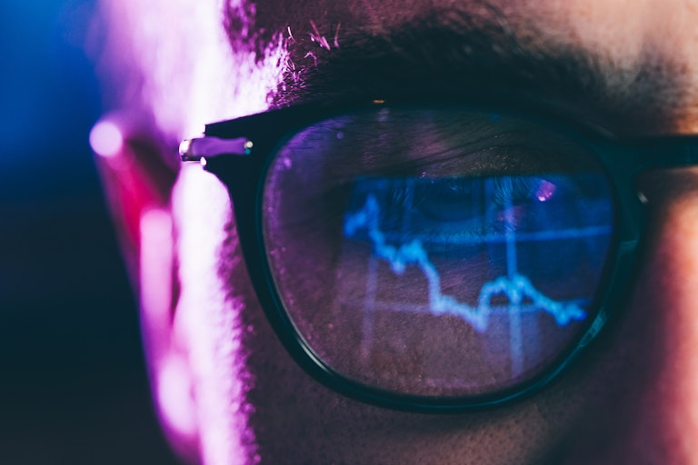 Close-up of a person's eye behind glasses reflecting a downtrending graph